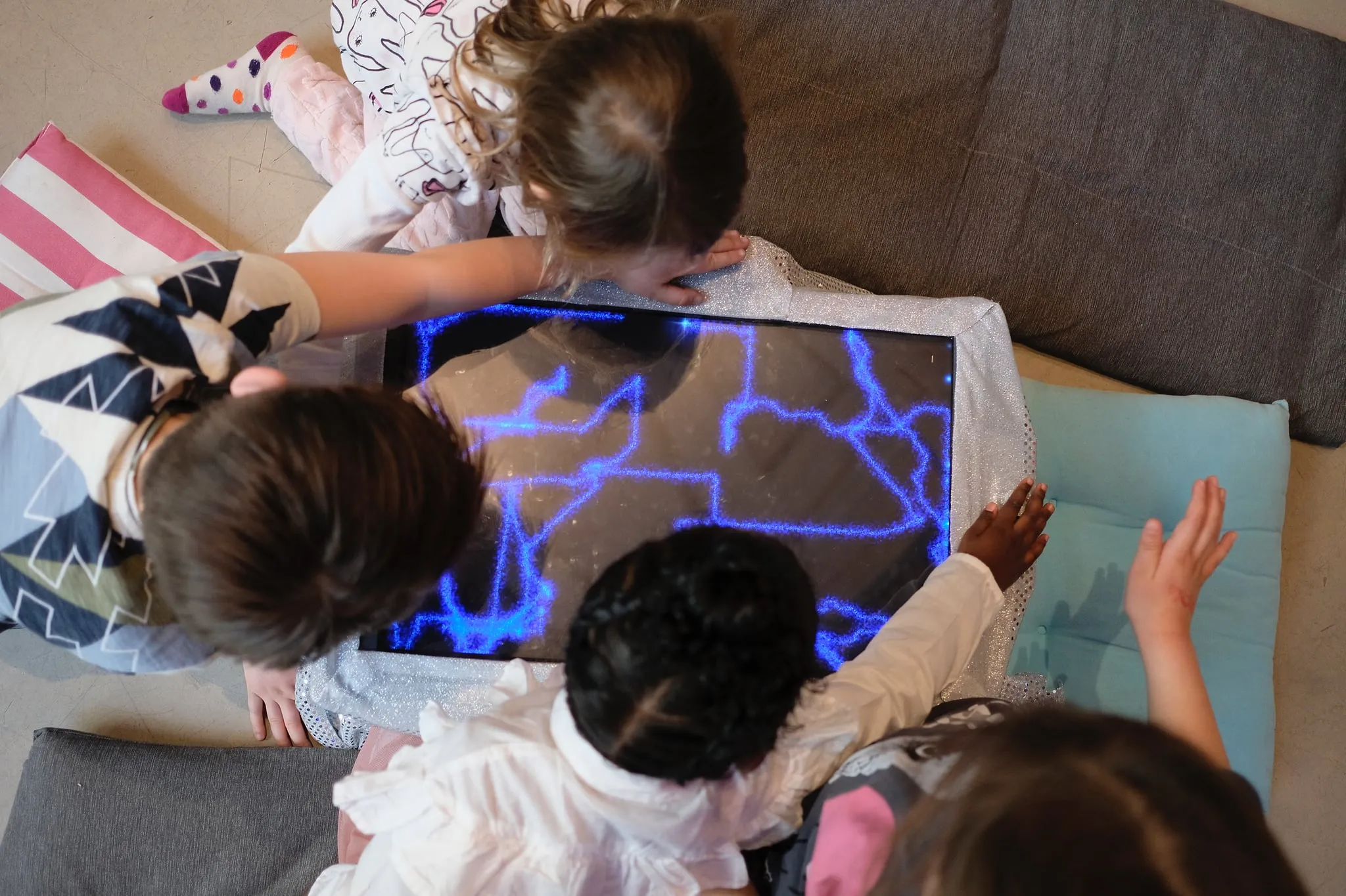 Kids hovering their hands over the edges of a screen displaying drawings from lines of stardust.