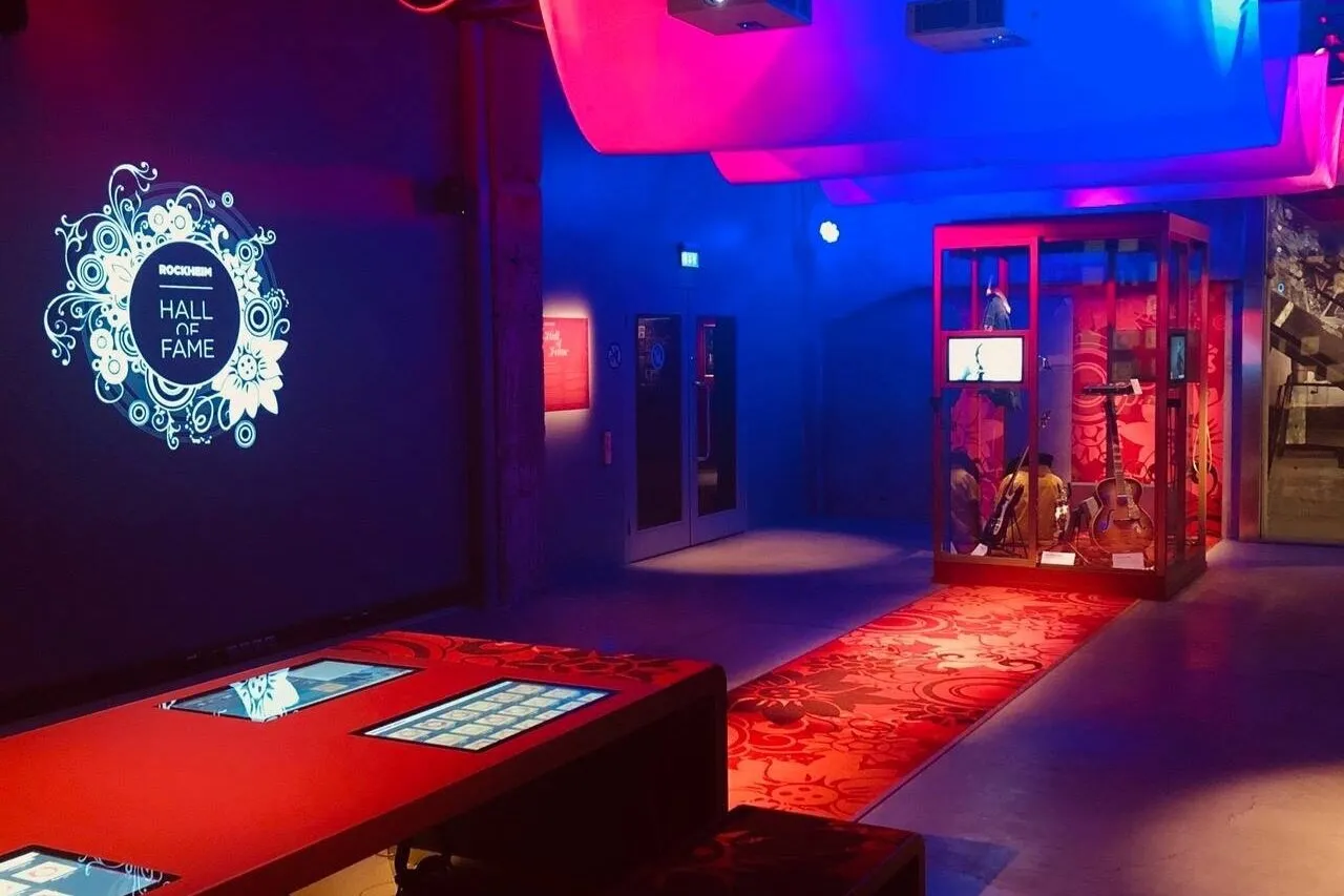 Room lit in strongly lights of strong red, purple and blue with a red carpet that connects into a table with touch screens on it